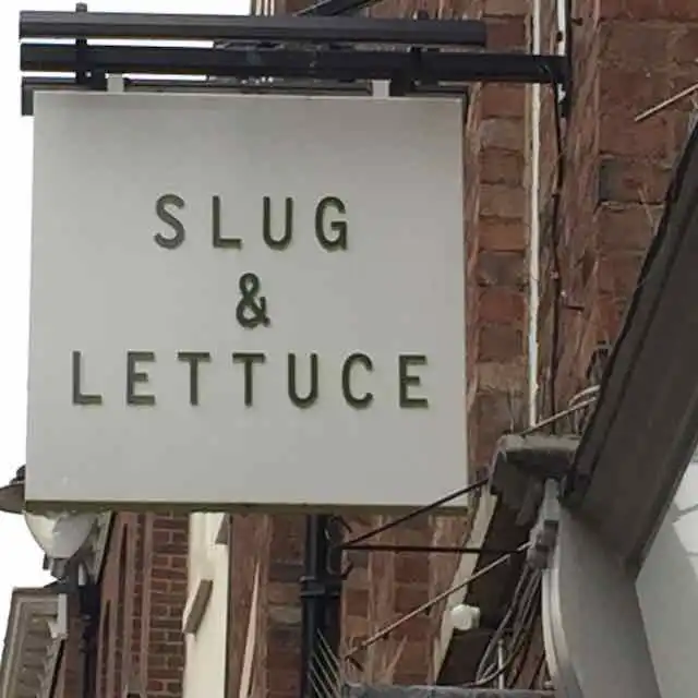 Sign hang above the sidewalk off a restaurant wall p. The sign says “Slug & Lettuce.”